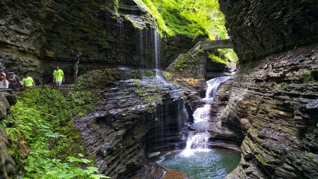 View of Watkins Glen State Park with a waterfall underneath a bridge and two tall rock faces on either side.