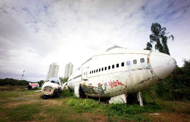 Two abandoned airplanes lay on grass side-by-side, two buildings far in the background.
