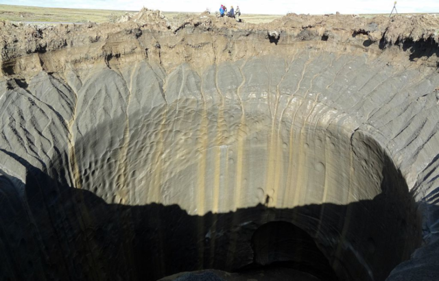 Aerial view looking down in the Sheregesh crater while a group of people look down from the edge.