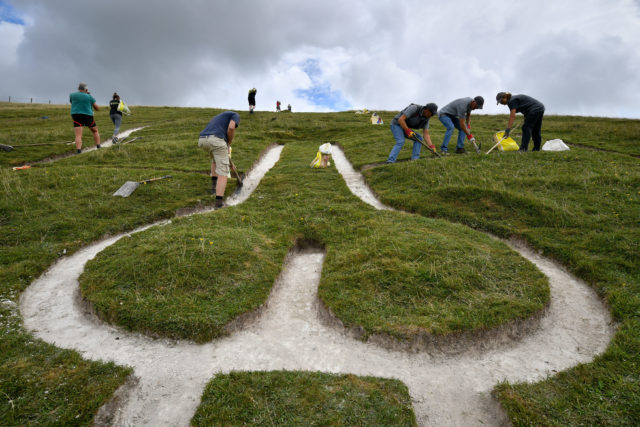 People cleaning a white pathway in lush green grass on a hillside.