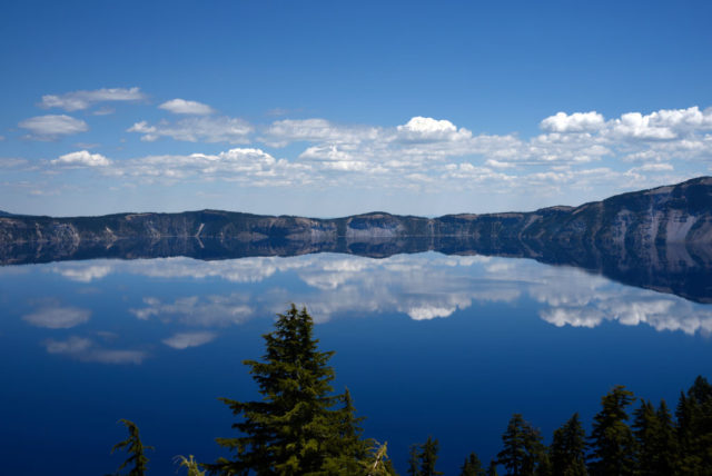 View looking out over Crater Lake with the clouds reflecting in the blue water.