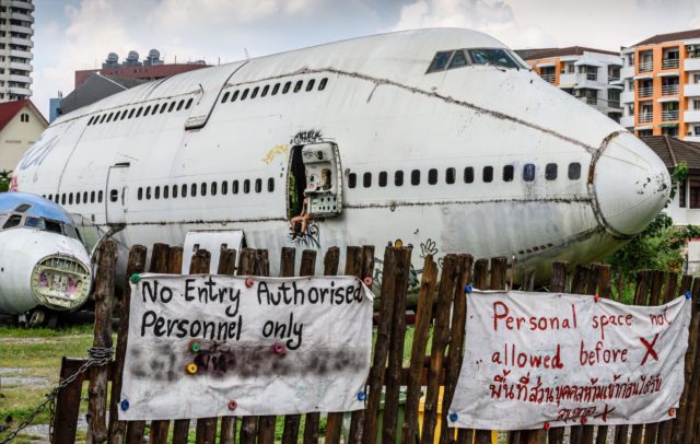 An abandoned airplane sits behind a wood fence with signs saying prohibited entry