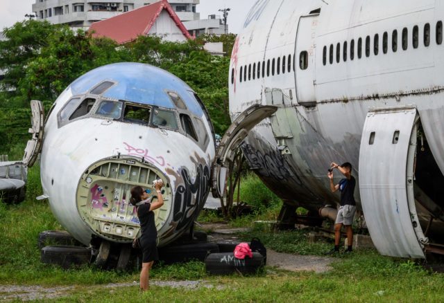 Tourists taking photos while standing beside two abandoned and decaying airplanes.