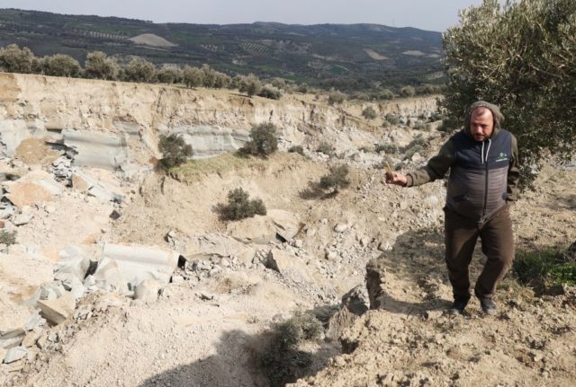 A man holds a cellphone over the large canyon that opened up in an olive grove