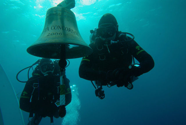 Two divers underwater beside the Costa Concordia bell.