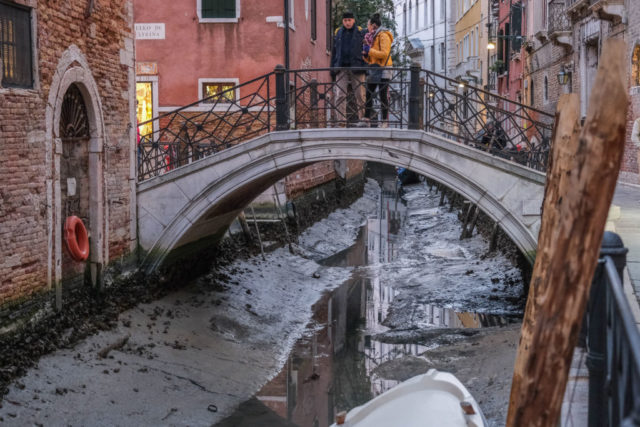 People look down at the empty canals from a bridge in Venice