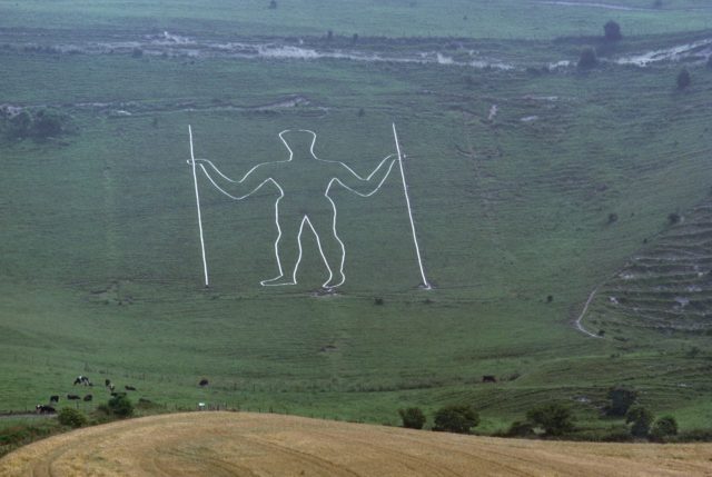 A figure of a man holding two staffs carved into a hillside.