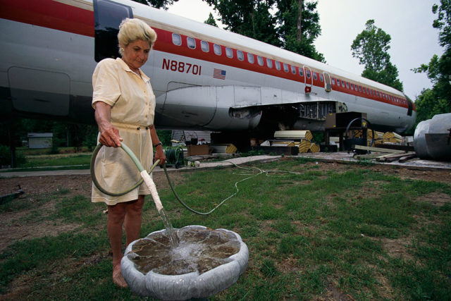 Jo Ann Ussery filling a birdbath with a hose with her plane home in the background.