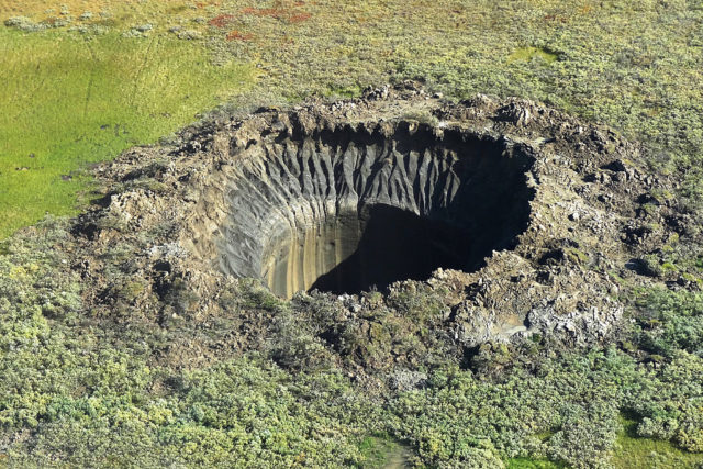 Aerial view of a crater in the middle of a grassy field. 