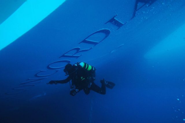Diver swimming beside the Costa Concordia logo on the ship underwater.