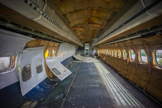 The interior of an abandoned plane, empty, with wall siding falling off.