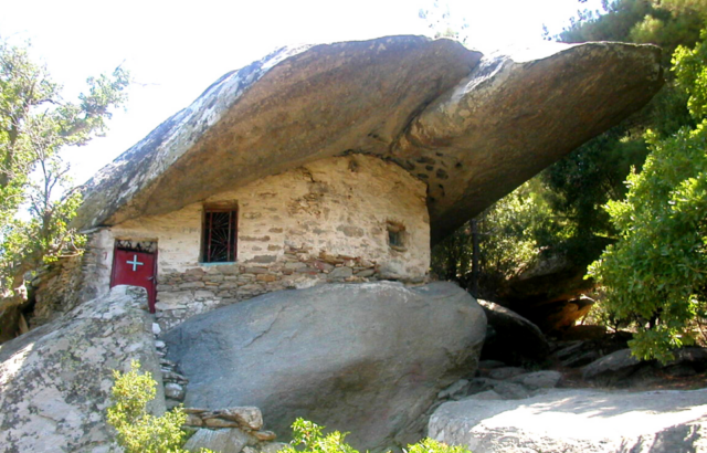 View of a house built inside / underneath a massive boulder, greenery surrounding it.