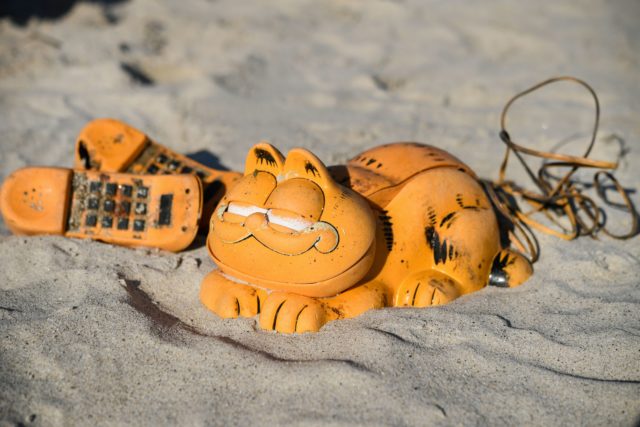 A battered Garfield phone lying on the sand. 