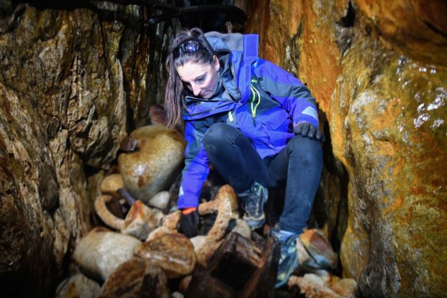 A woman crouching over rocks inside a cave.