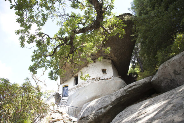A house fashioned from under a boulder, trees in the front.