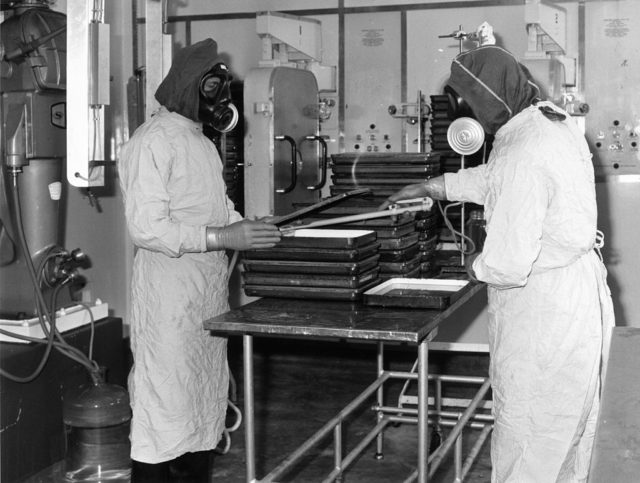 Two scientists wearing lab coats and masks conduct an experiment. 