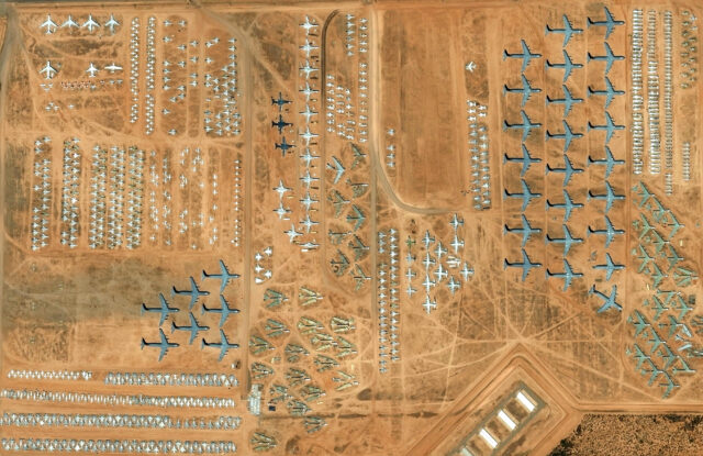 A satellite view of several military vehicles, largely aircraft, sitting in an airfield in like groups.