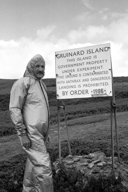 Man standing my a sign on Gruinard Island wearing full protective suit.