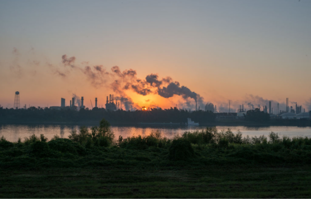 View of chemical plant with smoke rising into the air during a sunset.