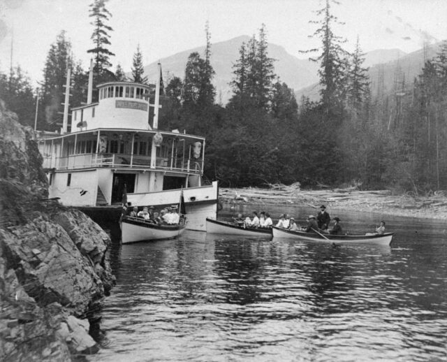 Wrecked sternwheeler surrounded by a group of people in canoes. 
