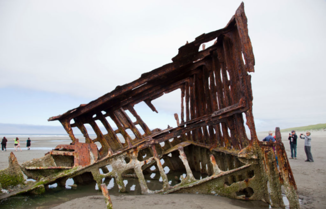 Piece of wrecked metal ship sticking up out of a sandy beach.