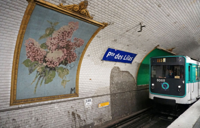 Métro train traveling through a station with a "Pte des Lilas" sign and a painting of a flower on the wall.