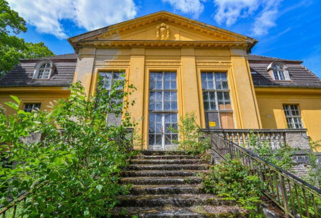 Looking up the stairs leading to a yellow building with large windows.