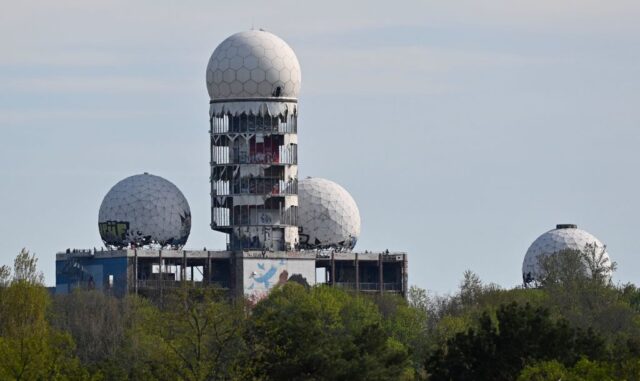 Abandoned Teufelsberg building peeking up above trees, with four white spheres on top. 