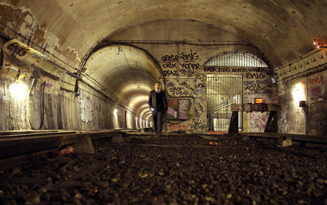 Man in a suit walking through a Métro tunnel with graffiti on the walls.