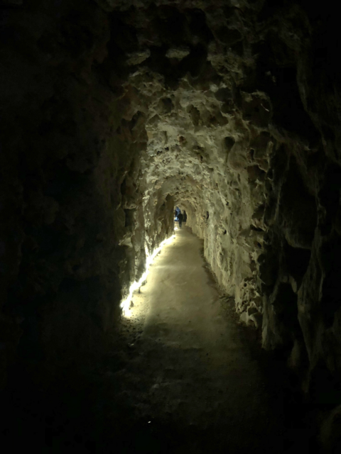 A stone tunnel lined with LED lighting on the ground/
