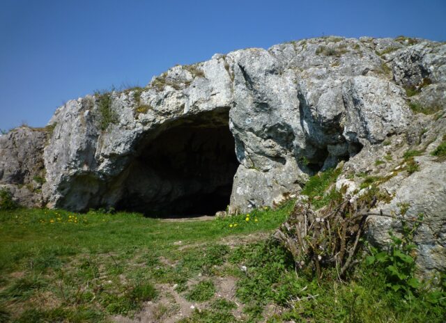 A stone cave sitting at the top of a hill with a circular opening.