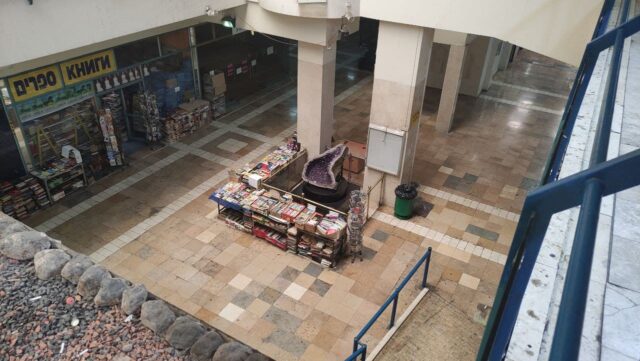 Looking down toward an empty floor, a kiosk and a store front.