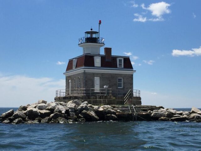 A house surrounded by rocks and water, a lighthouse sticking out the top