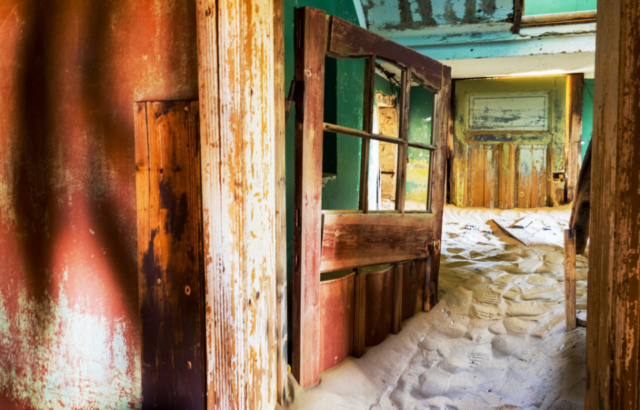 Inside of a house with a wooden door, with the floor covered in a pile of sand.