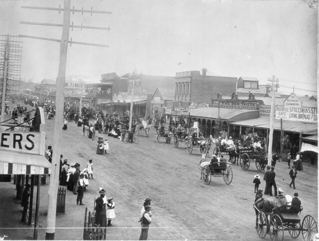 A bustling street with people walking and on horse-drawn carts.