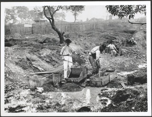 Men mining in a field with wooden equipment.