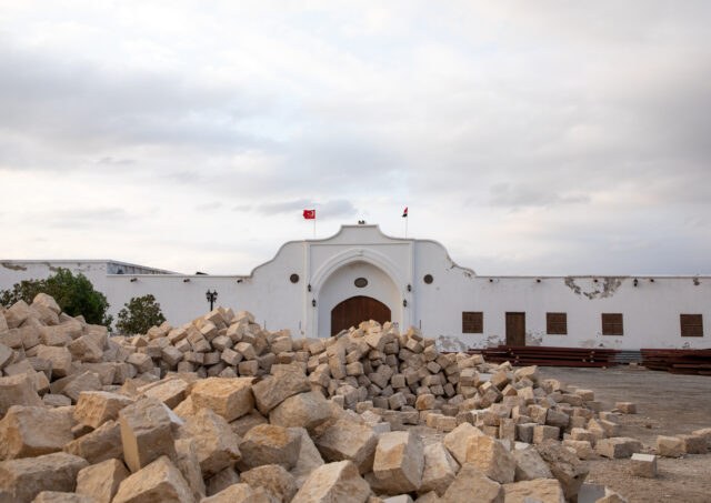 A wide white building in the background, a pile of rubble in the foreground.