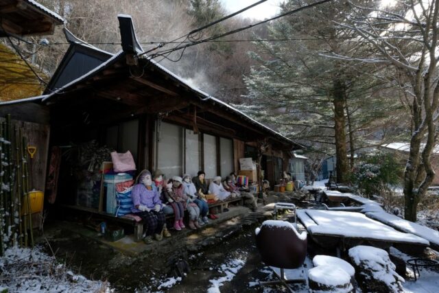 Group of dolls placed on the front porch of a building.