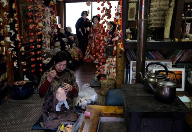 Tsukimi Ayano sitting on her knees while sewing the head of a doll.