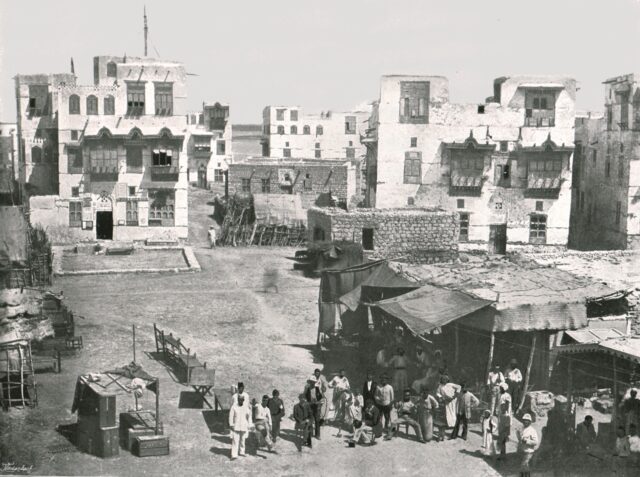 A photograph of buildings in Suakin, people gathered in front of a small building.
