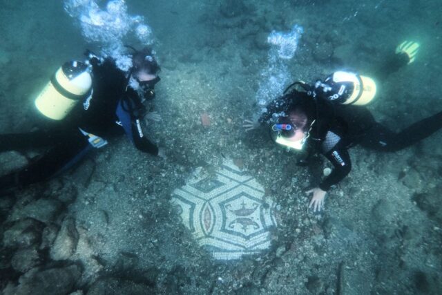 Two divers brushing off an underwater mosaic.