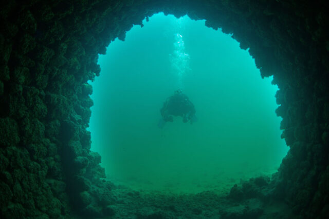 Diver swimming through an underwater ruin.
