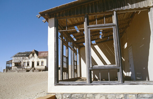 Close-up view of an abandoned building with large windows, with a second building in the background.