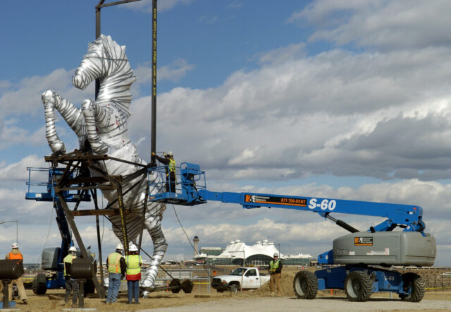 A horse sculpture wrapped in plastic wrap for safety, is being moved by a lift.