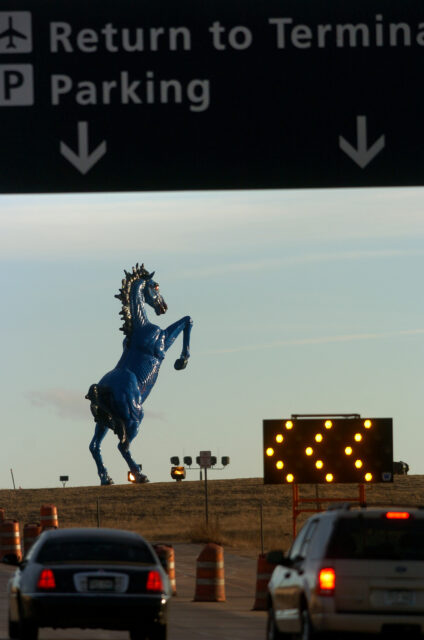 The "Mustang" sculpture seen in the background, a sign overhead with cars approaching it and a lighted sign indicating to go left.