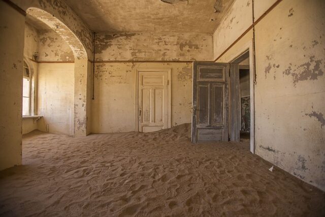 Large spacious room with an open door, filled with sand on the floor.