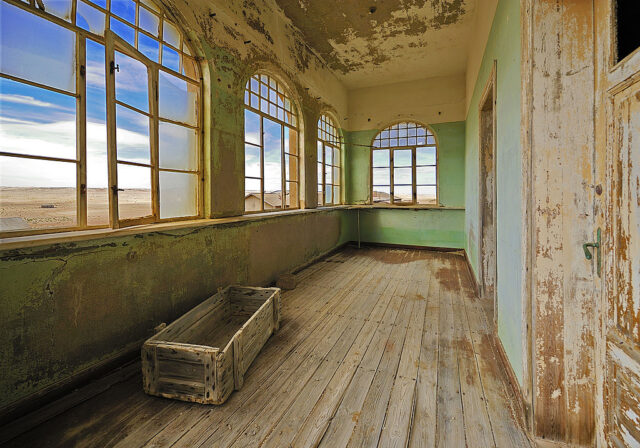 Wooden room with multiple arched windows and paint peeling off the walls.