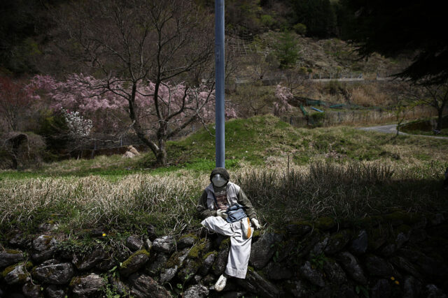 Doll with crossed legs sits on the bank of a river.