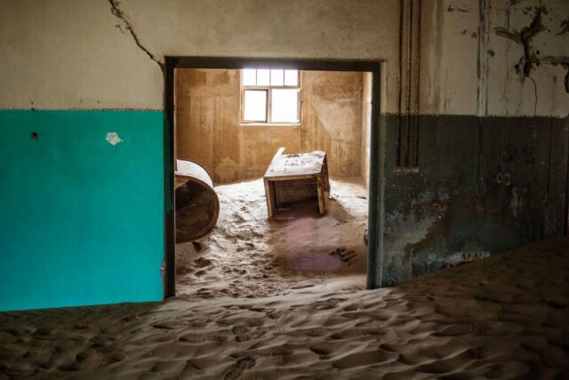 View through a doorway into a room filled with sand, with furniture sitting on top.