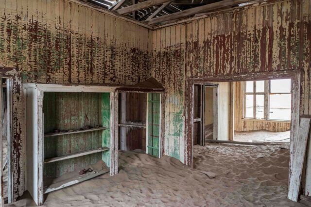 Wooden room with wooden shelving, filling with sand on the floor.